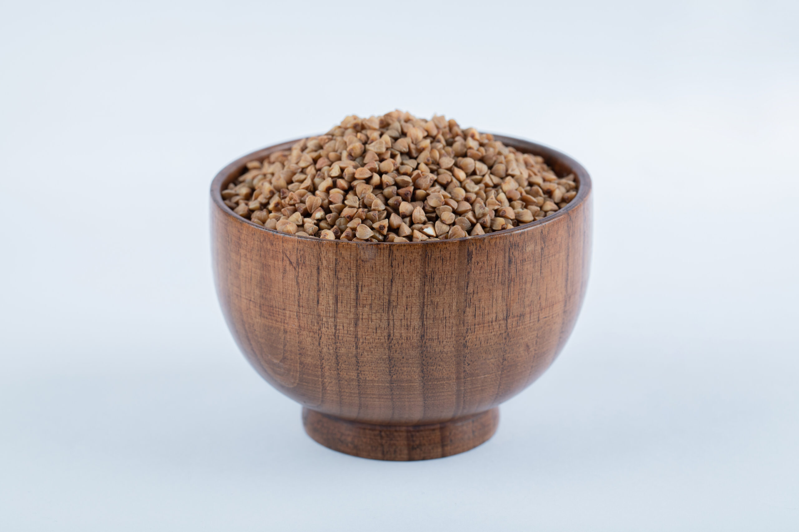 a small wooden bowl full of buckwheat on white background