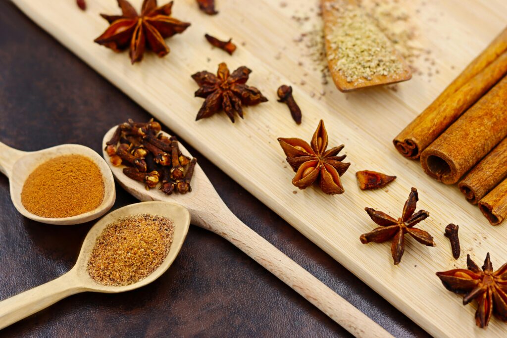 Aromatic star anise, cinnamon, and cloves arranged with spoons on a wooden board.