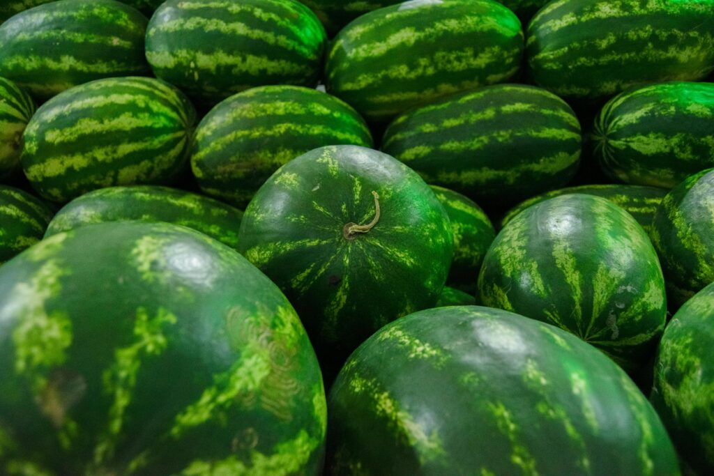 Pile of fresh watermelons glistening under market lights, showcasing nature's vibrant patterns.